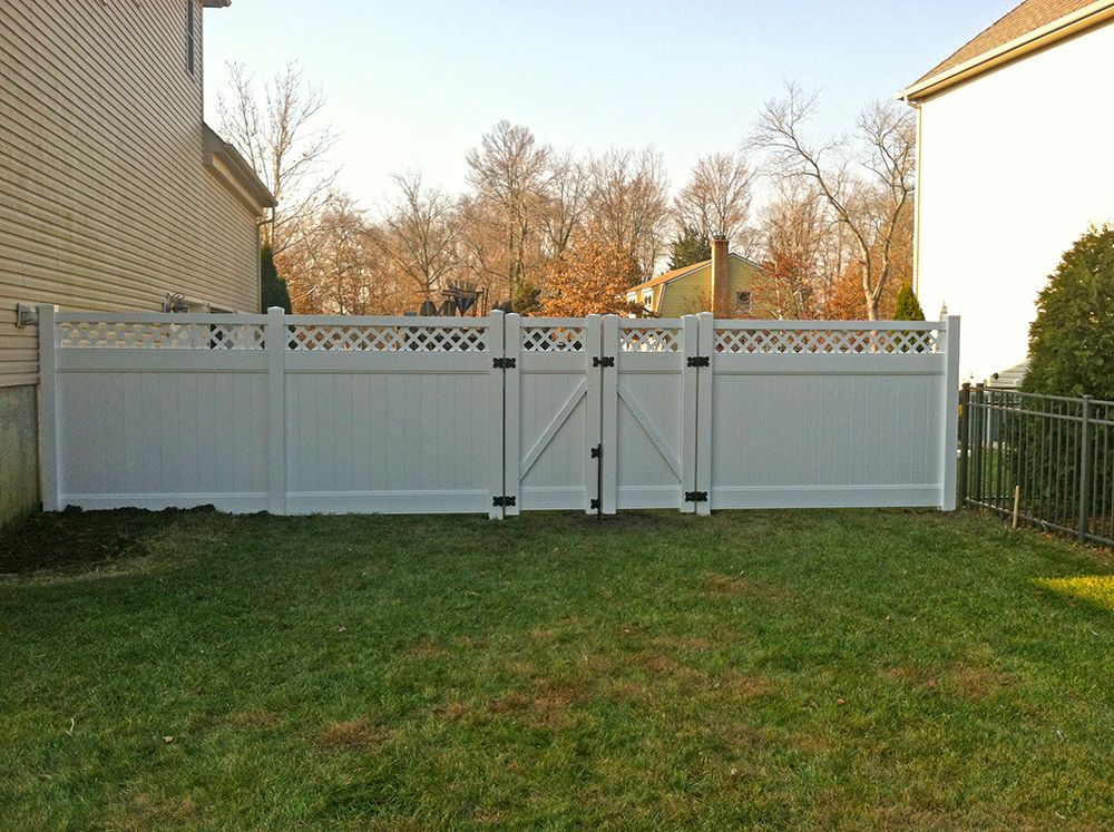 White vinyl fence with gate in a backyard, flanked by houses and a grassy lawn.