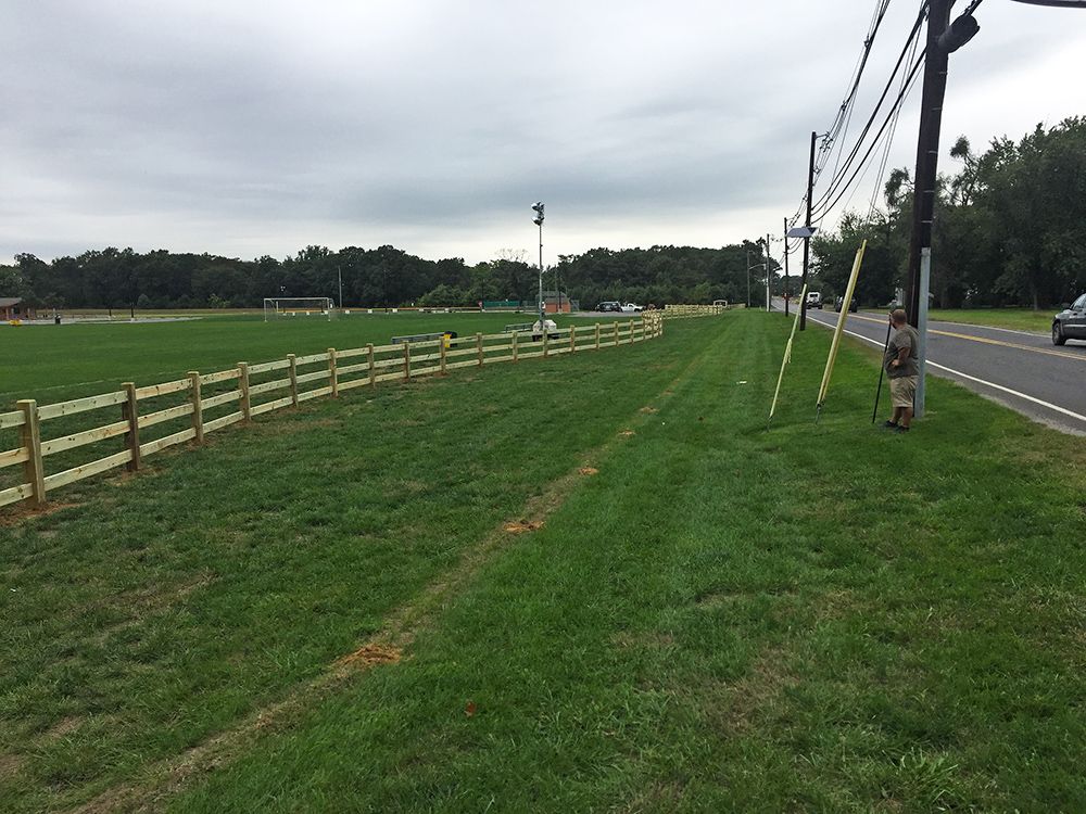 Wooden fence lines a grassy field next to a road under an overcast sky.