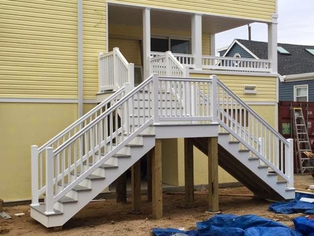 White stairs leading to a yellow house with a porch. Stairs are supported by wooden posts.