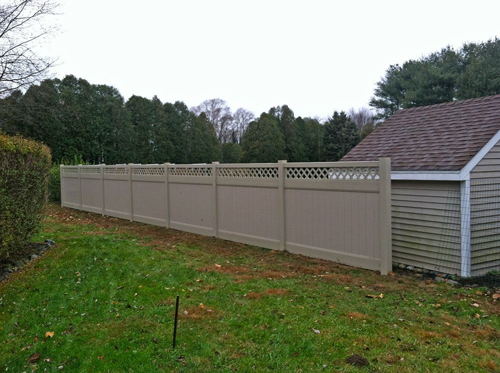 Tan privacy fence alongside a grassy yard, next to a building and trees.