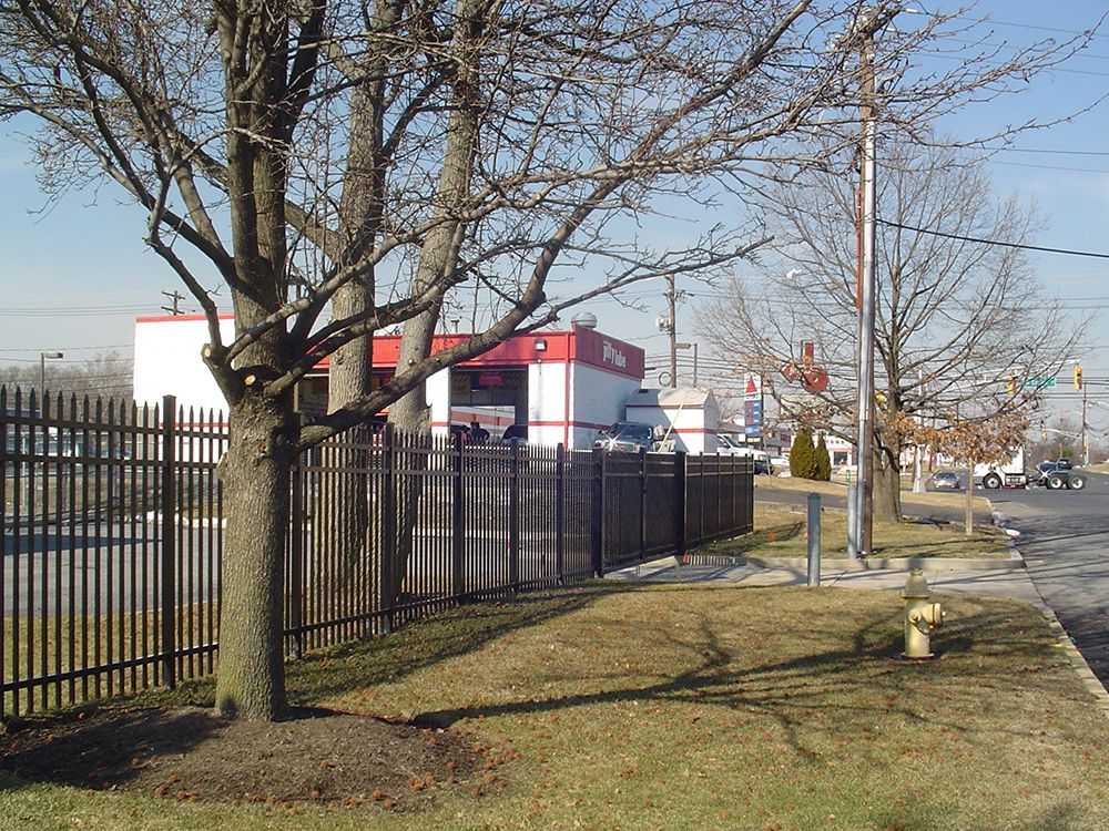 Metal fence in front of a building with a red and white facade. Bare trees, a road, and blue sky in the background.