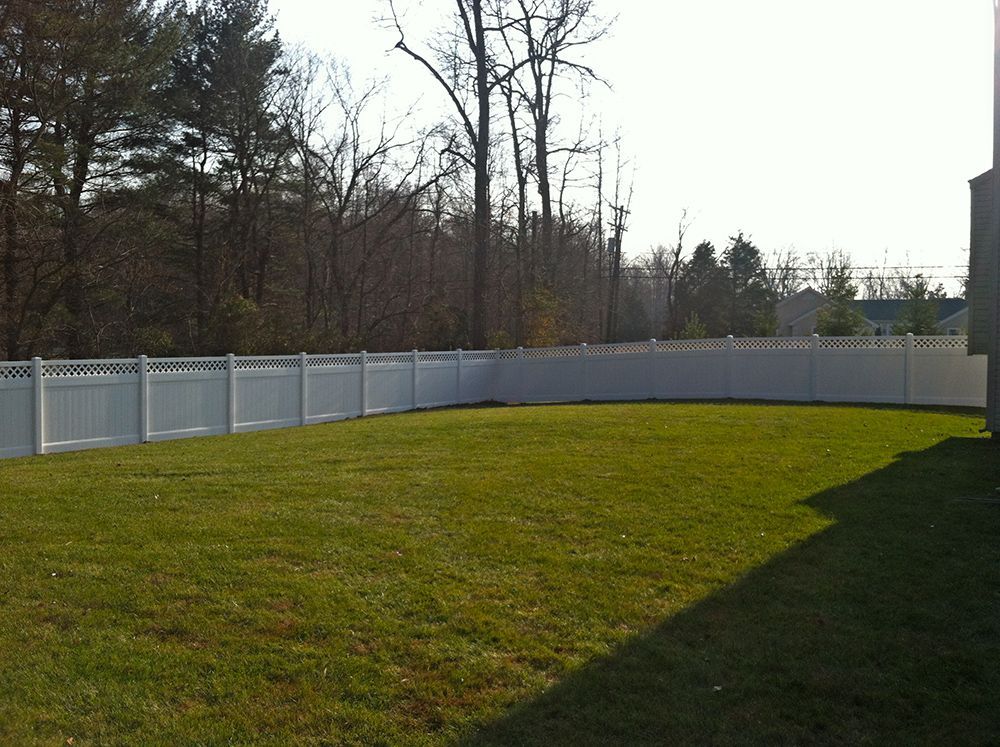 White fenced backyard with green grass and trees in the background.