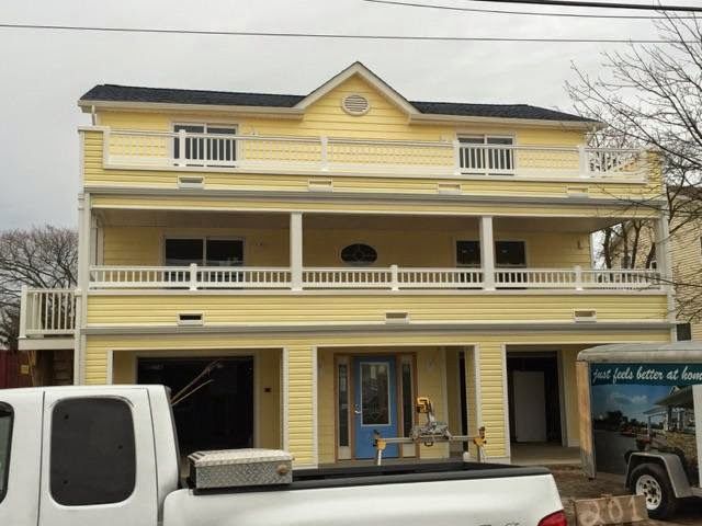 Yellow two-story house with blue door, white railings, and a black roof. A white truck is in front.