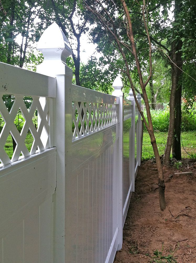 White vinyl fence with lattice and finials, set in a backyard with trees and grass.