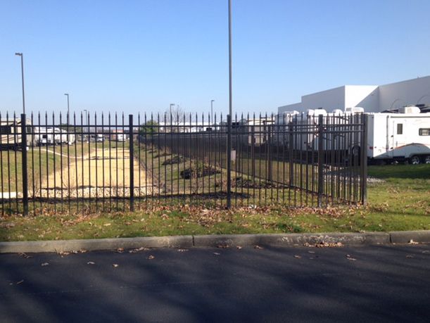 Black metal fence bordering a vacant lot, with a building in the background.