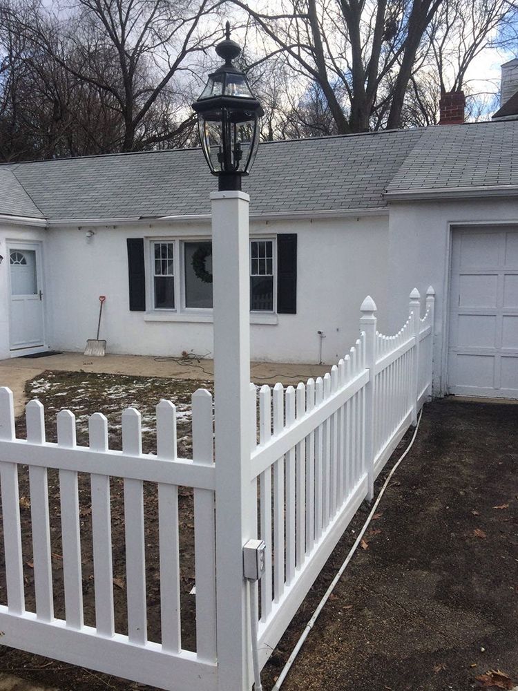 White picket fence with a lighthouse-style lamp post in front of a white house with black shutters.