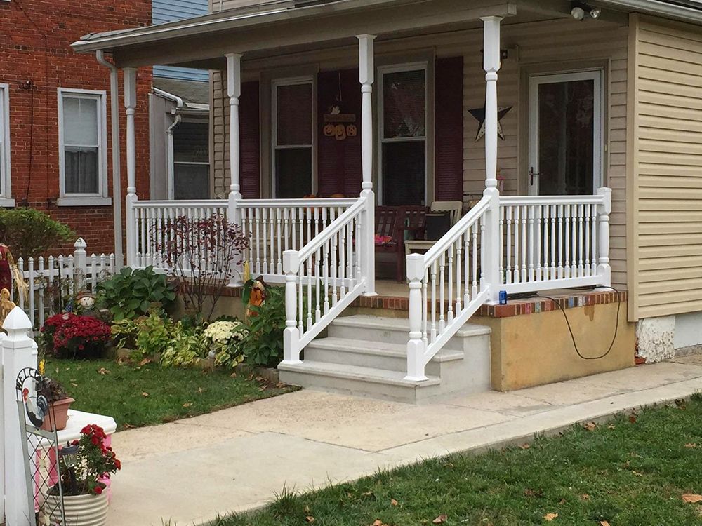 White porch with railings, steps, and a walkway leading to a house with beige siding and a red front door.