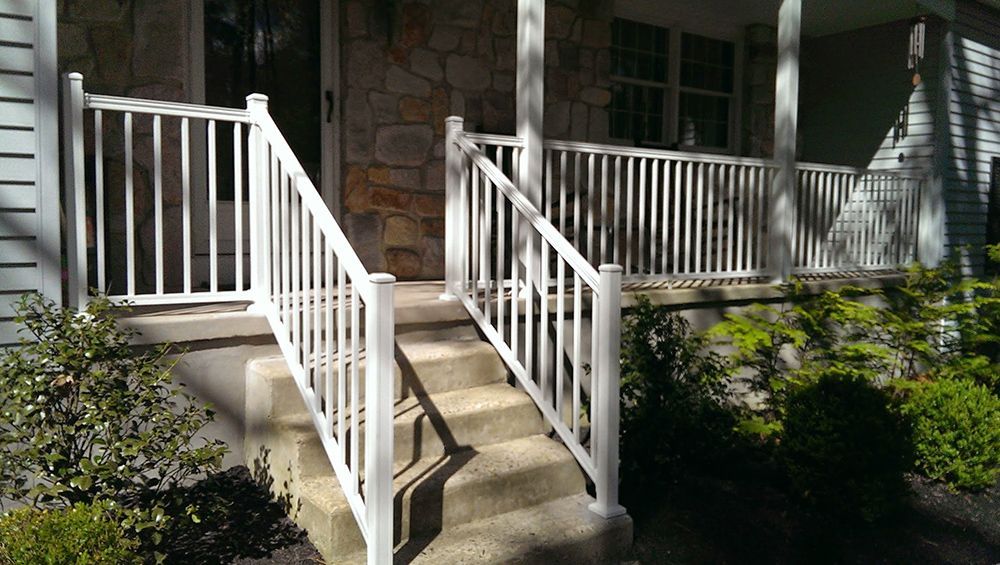 White porch with railings and steps leading up to the front door of a home with stone facade.