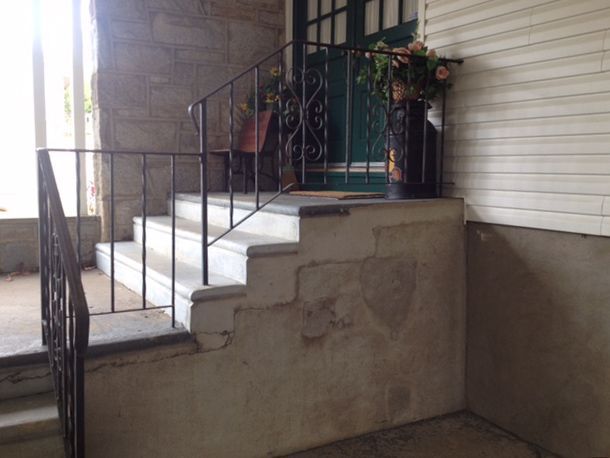 Exterior steps leading to a green door, featuring a black railing and potted plants.