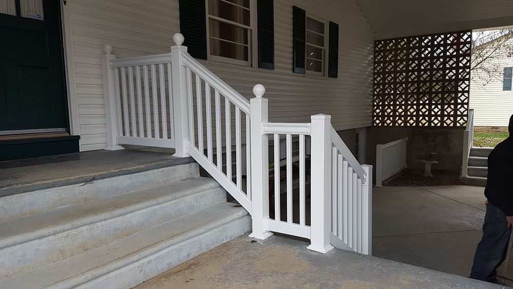 White railing and steps leading up to a house. A person stands on the right.