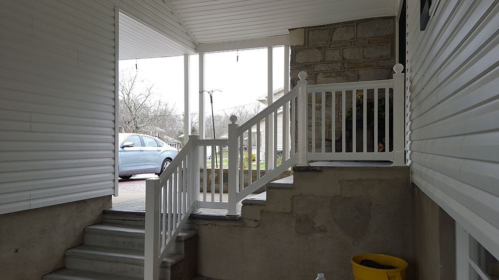 White railing and stairs leading up to a porch, with a car visible in the background.