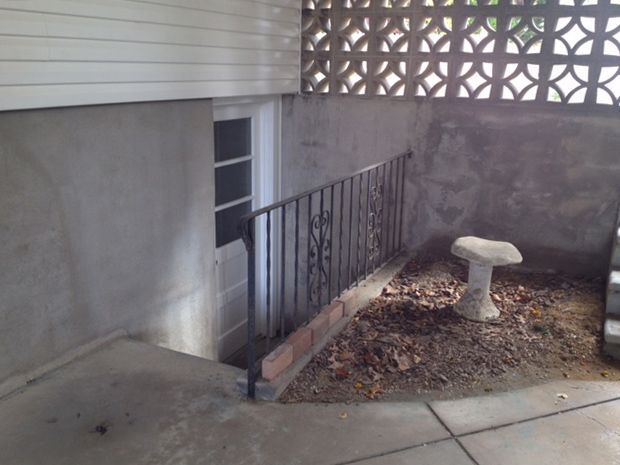 Exterior basement doorway with railing and small garden, cement and brick.
