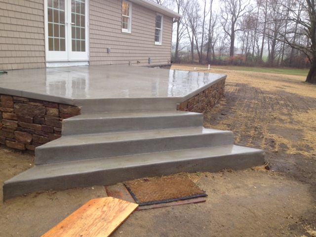 Concrete steps leading up to a patio. The patio has a stone retaining wall and is next to a house.