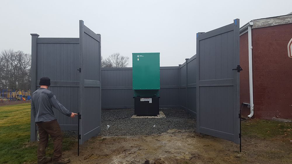 Man opening grey fence gates to a green electrical box surrounded by grey fencing.