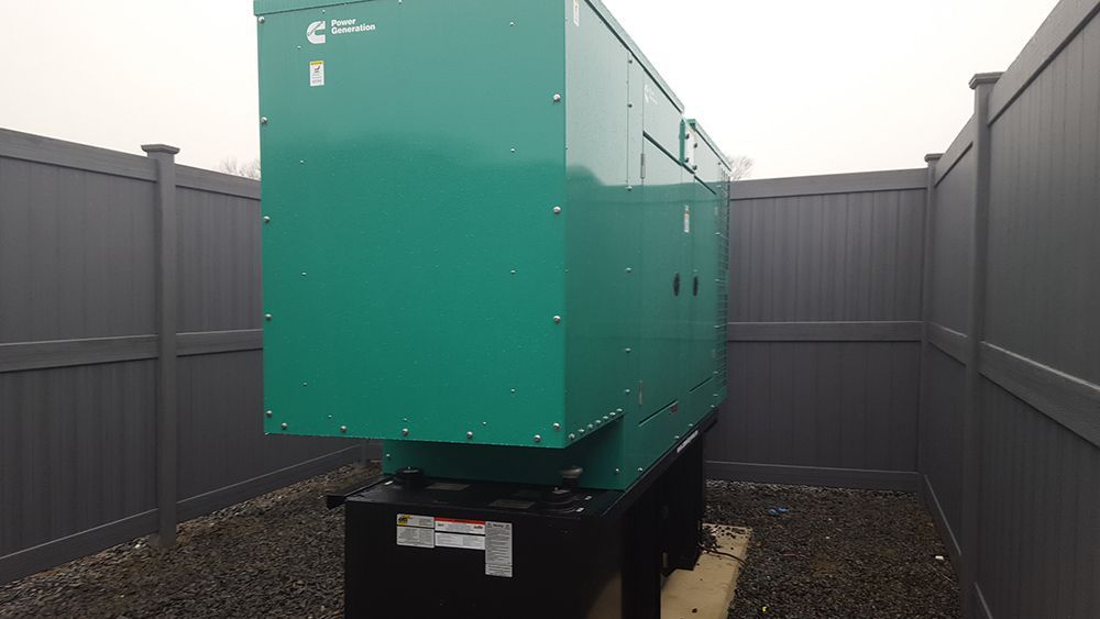 Green industrial generator in a fenced enclosure.