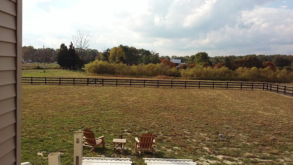 Overlooking a brown field with a wooden fence and trees under a cloudy sky. Two chairs are in the foreground.