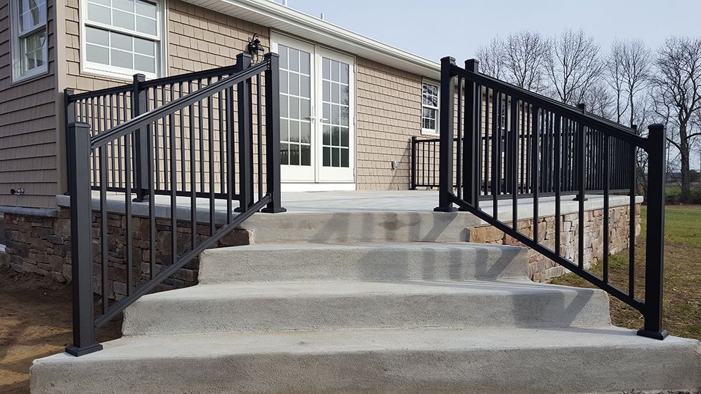 Concrete steps leading to a deck with black metal railings, in front of a house.
