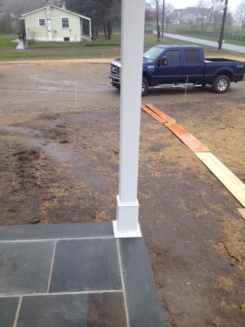 White porch column on a slate tile porch. A blue truck parked on a dirt driveway is in the background.