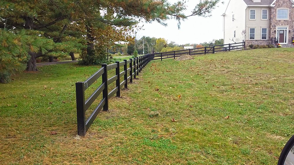 Black wooden fence along grassy lawn, curving toward a beige house.