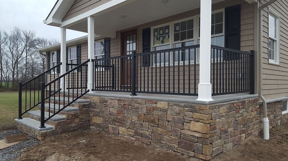 A house with a stone and brick front porch and black railings, on a cloudy day.