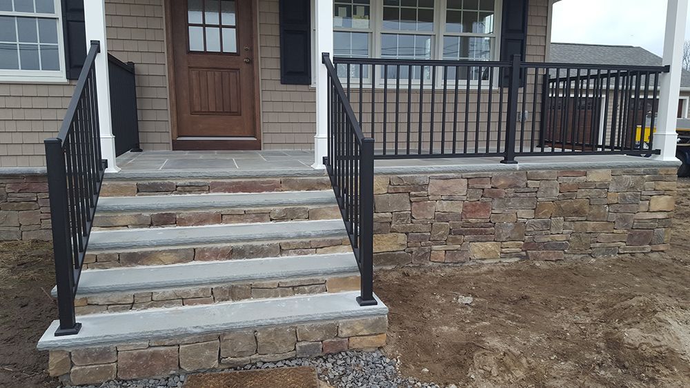 Stone steps with black railing leading to a house entrance. Brown and tan stone facade.