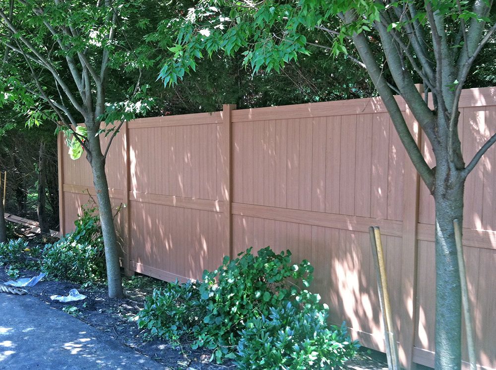Brown wooden fence bordered by trees and shrubs.