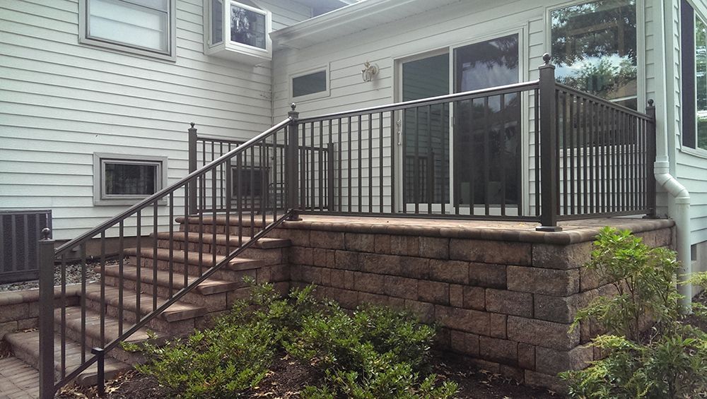 Outdoor patio with brick retaining wall, dark railing, steps, and sliding glass door.