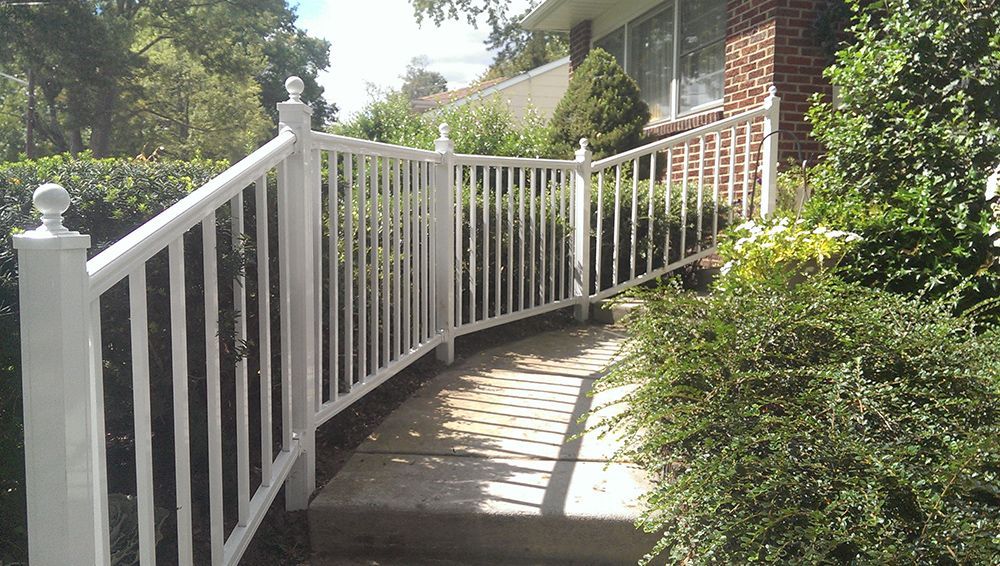 White railing along a curved pathway leading to a brick house entrance.