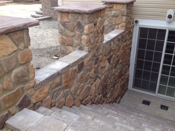 Stone steps leading down to a basement door, framed by stone walls and topped with concrete caps.