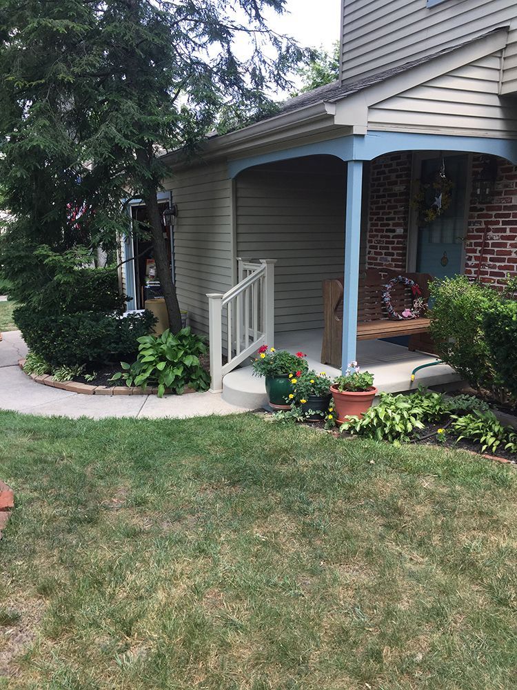 A beige house with a porch and blue trim, featuring landscaping and a sidewalk.