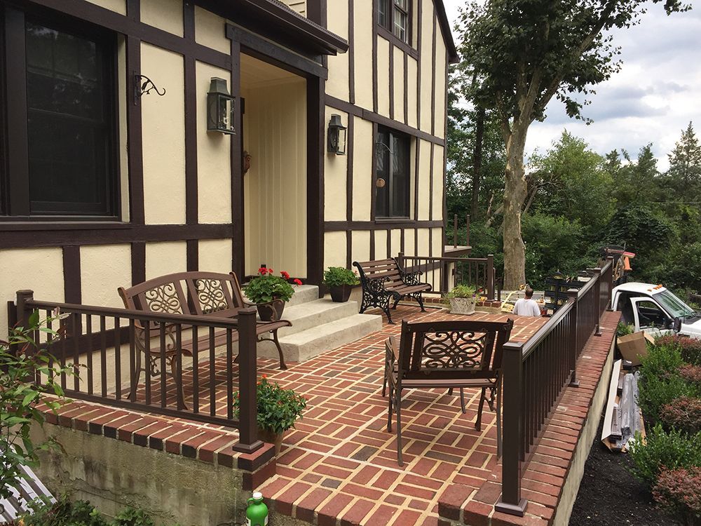 Tudor-style house with brick patio, brown trim, and decorative metal furniture.