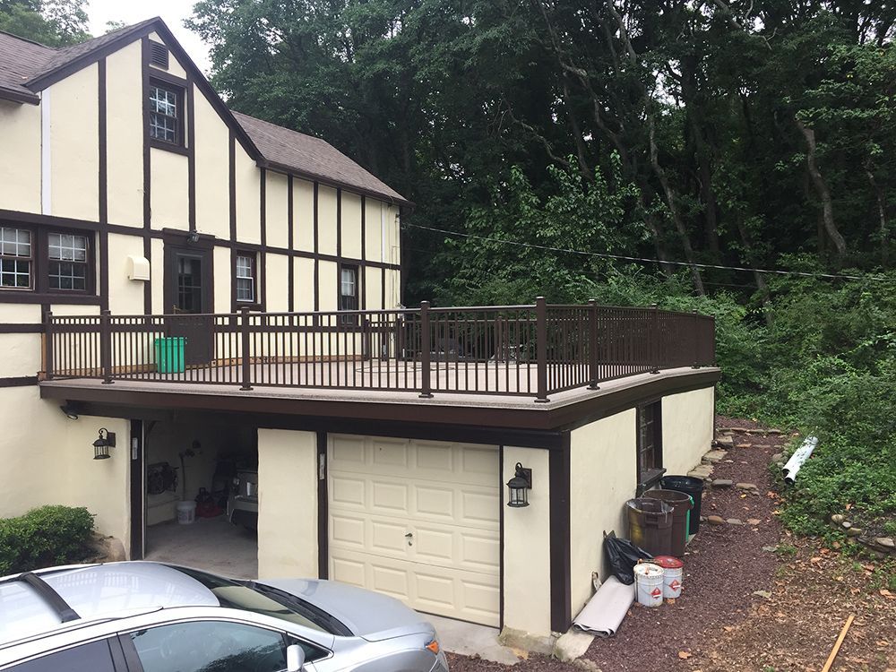 Two-story house with a deck above garage. Beige exterior, brown trim, and a car parked in front.