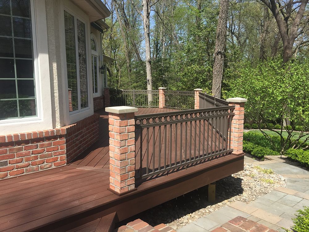 Deck with brick columns, brown railing, and adjacent landscaping.