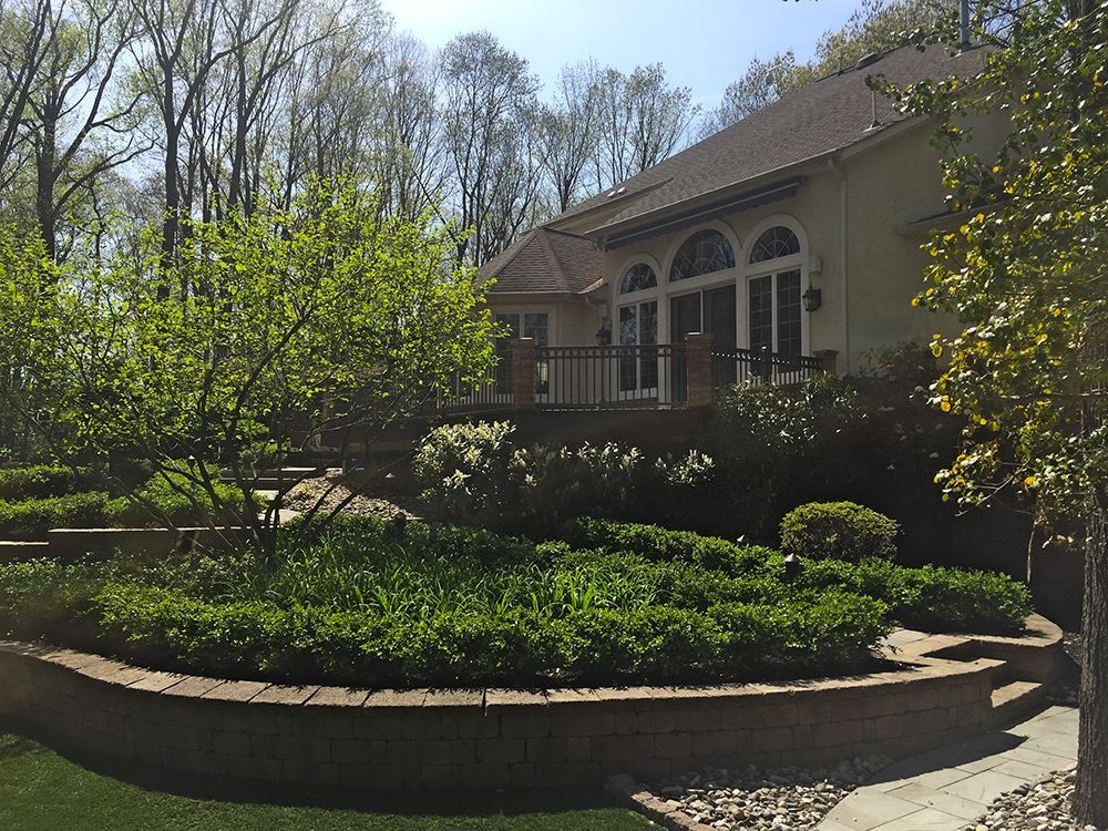 Backyard landscaping with terraced flower beds and a house with a deck.