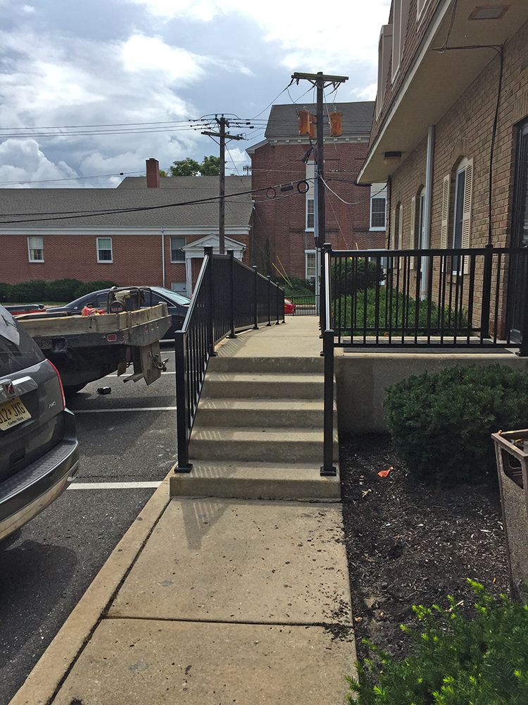 Concrete stairs with black railing leading to a building's entrance. A sidewalk and parked cars are in view.