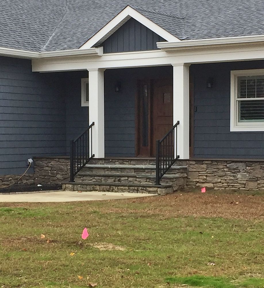 Blue house with stone steps and porch, black railings, and white columns.