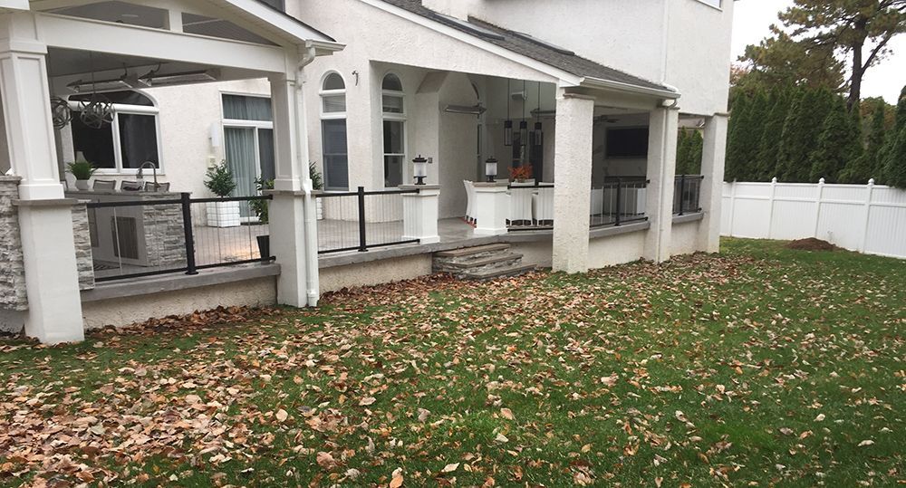 Backyard with covered patio, stone and white stucco house. Fallen leaves on grass.