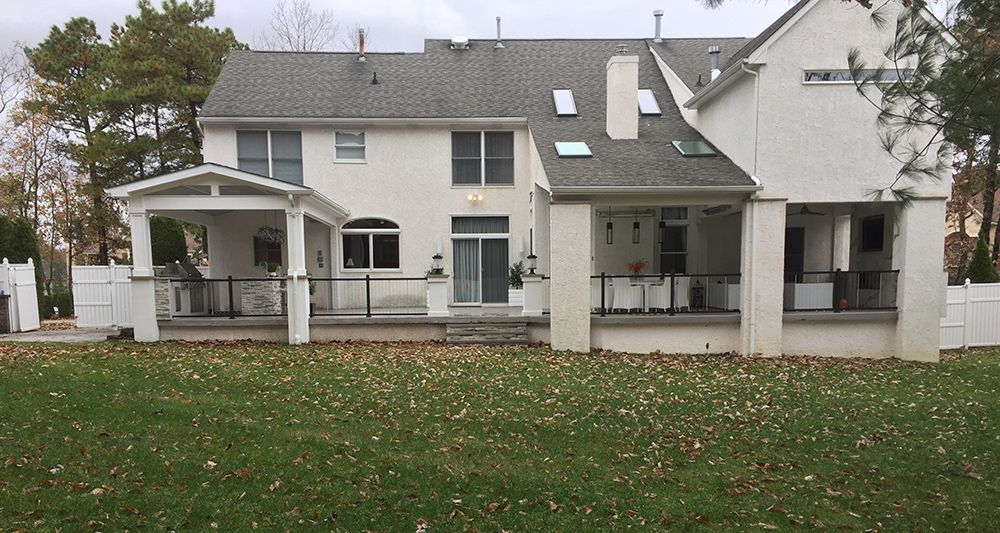 Back of a white house with a covered patio and a grassy lawn with fallen leaves.