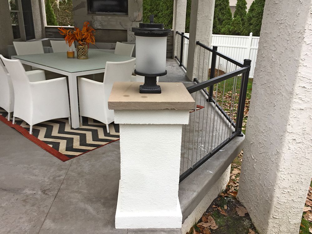 White pillar with a lamp on top, porch with dining set and black railing.