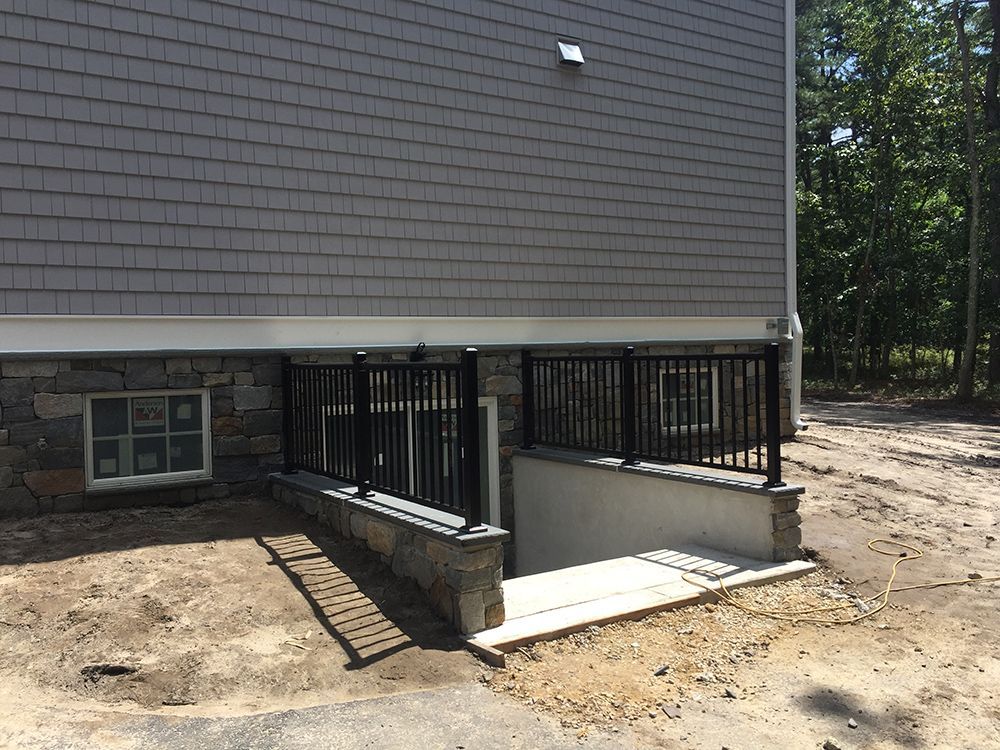 Exterior view of a building with stone foundation, entry steps, black railing, and gray siding.