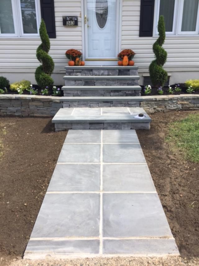 Stone walkway and steps leading to a house with a white door, topped with autumn decorations and two spiral topiaries.