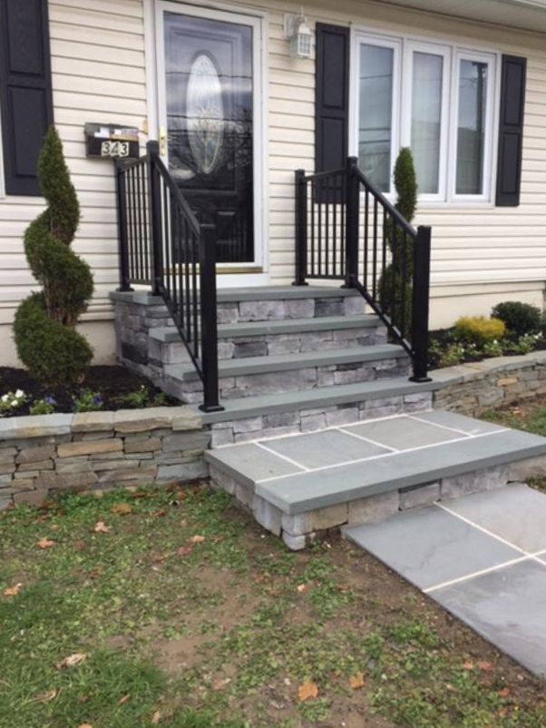 Stone steps leading to a house entrance with black railing and manicured landscaping.