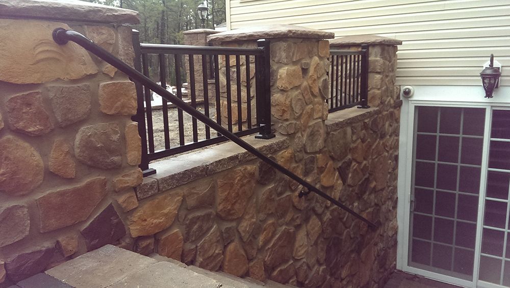 Stone wall with black railing and handrail leading to a sliding glass door.