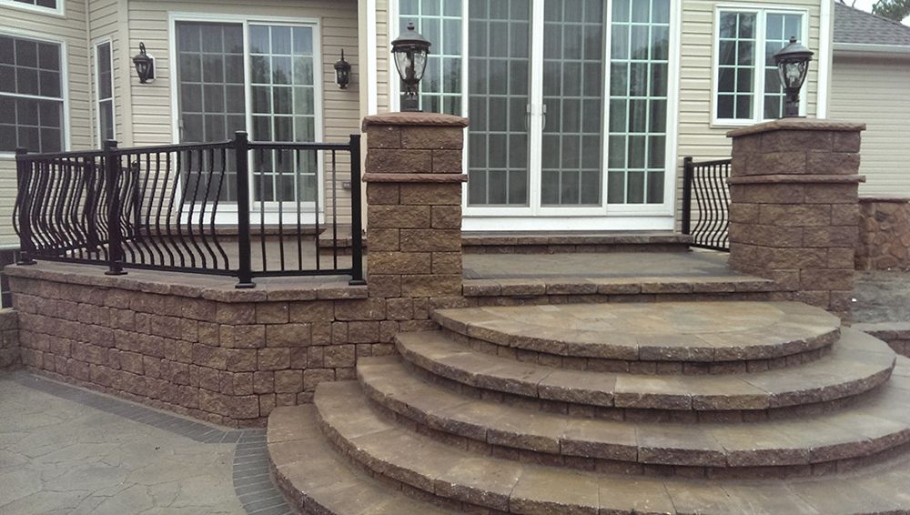 Stone patio with curved steps, brick walls, black wrought iron railing, and sliding glass door.