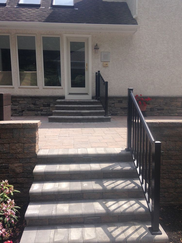 Stone steps leading up to a patio and door, with black handrails and a brick accent wall.