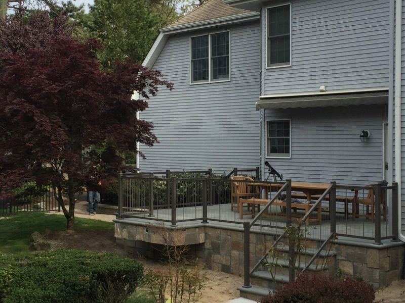 Exterior view of a house with a raised deck, stone facade, and a red Japanese maple tree.