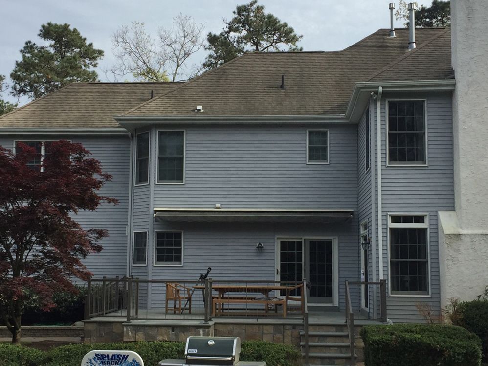 Back view of a two-story blue house with deck and red tree in the yard.