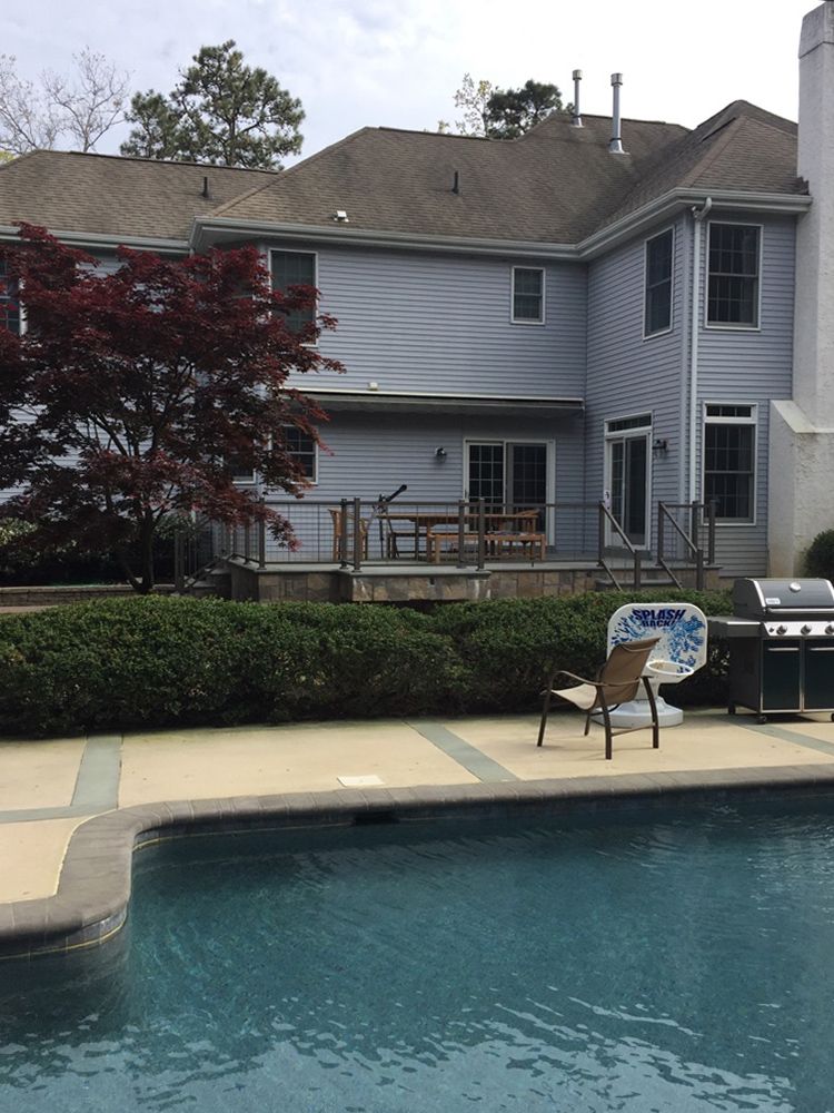 Back of a house with a pool in the foreground. Deck and patio furniture are visible. Red tree on the left.