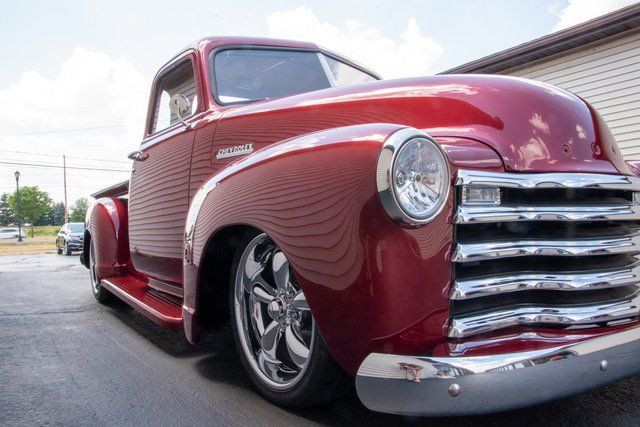 Red classic Chevrolet pickup truck with chrome details parked outdoors.