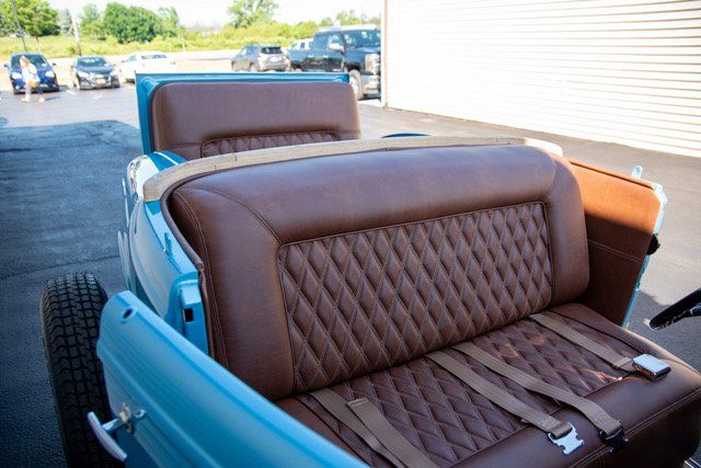 Blue classic car interior with brown quilted leather seats and tan seatbelts.